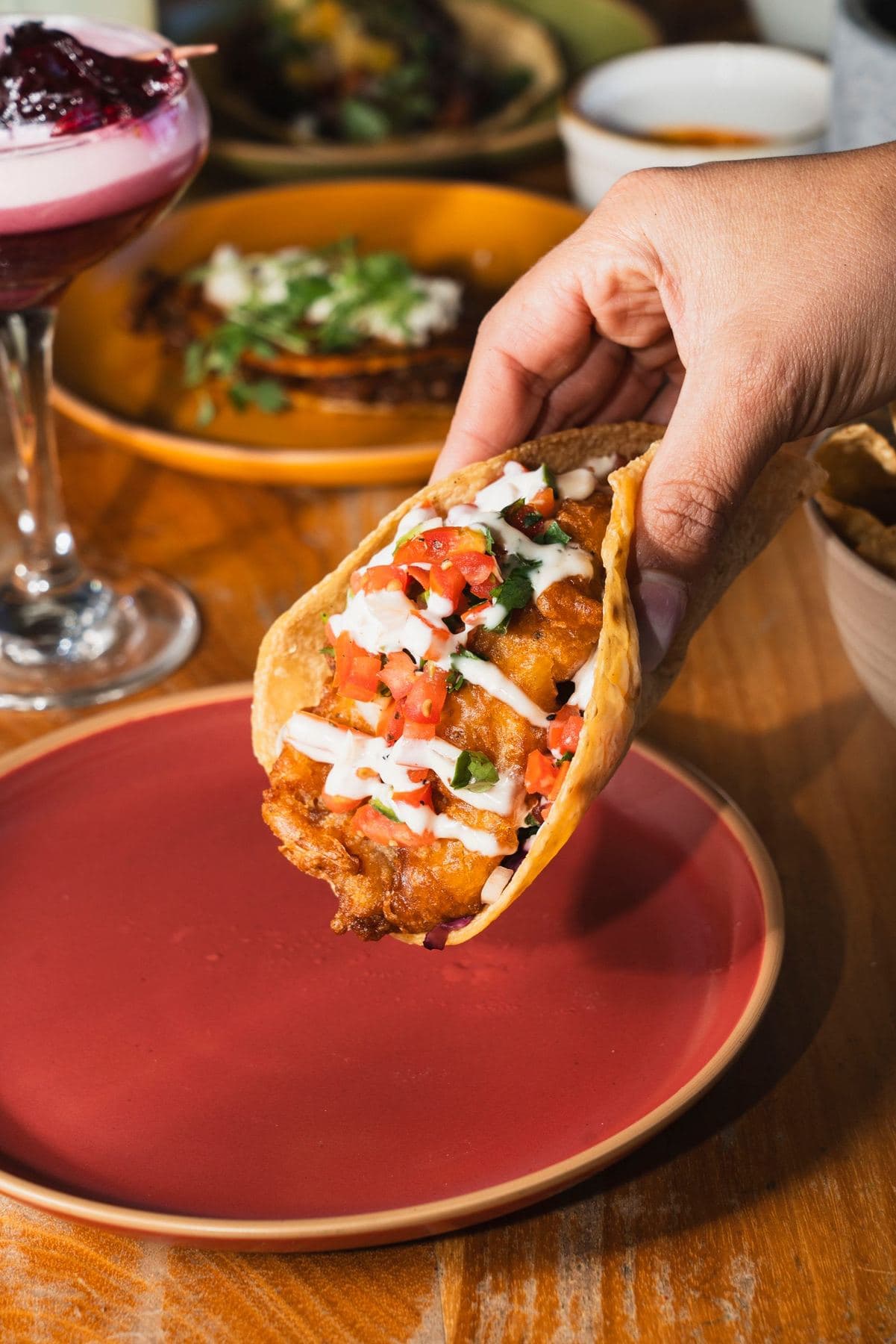 Hand holding a beer-battered Baja fish taco topped with crema and salsa fresca