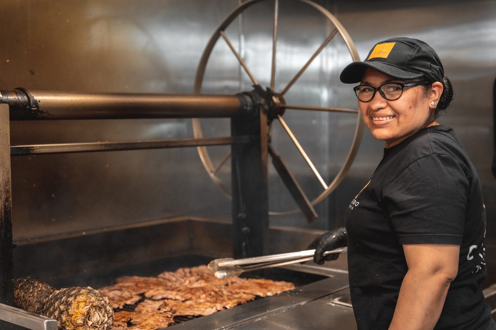 Cook smiling beside the grill as meat sears