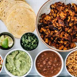 Pollo asado family-style taco kit with tortillas, guacamole, beans and rice