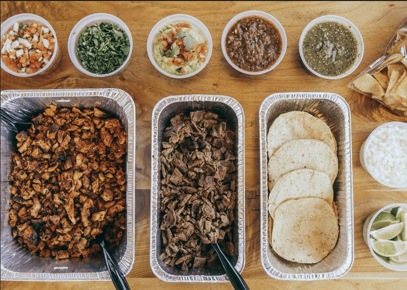 Taco bar catering spread with grilled meats, tortillas and salsas