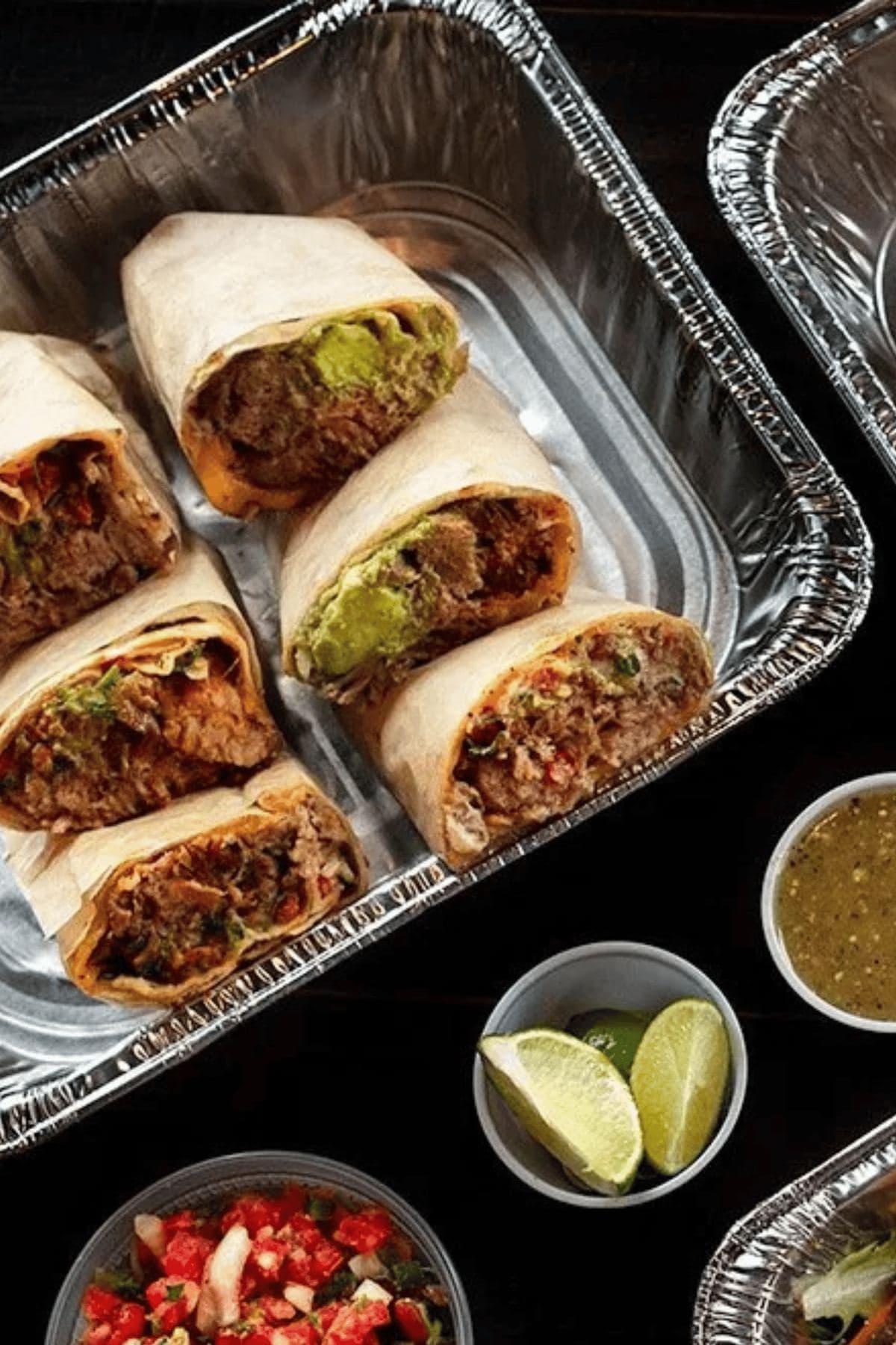 Catering tray of halved burritos with limes and salsa