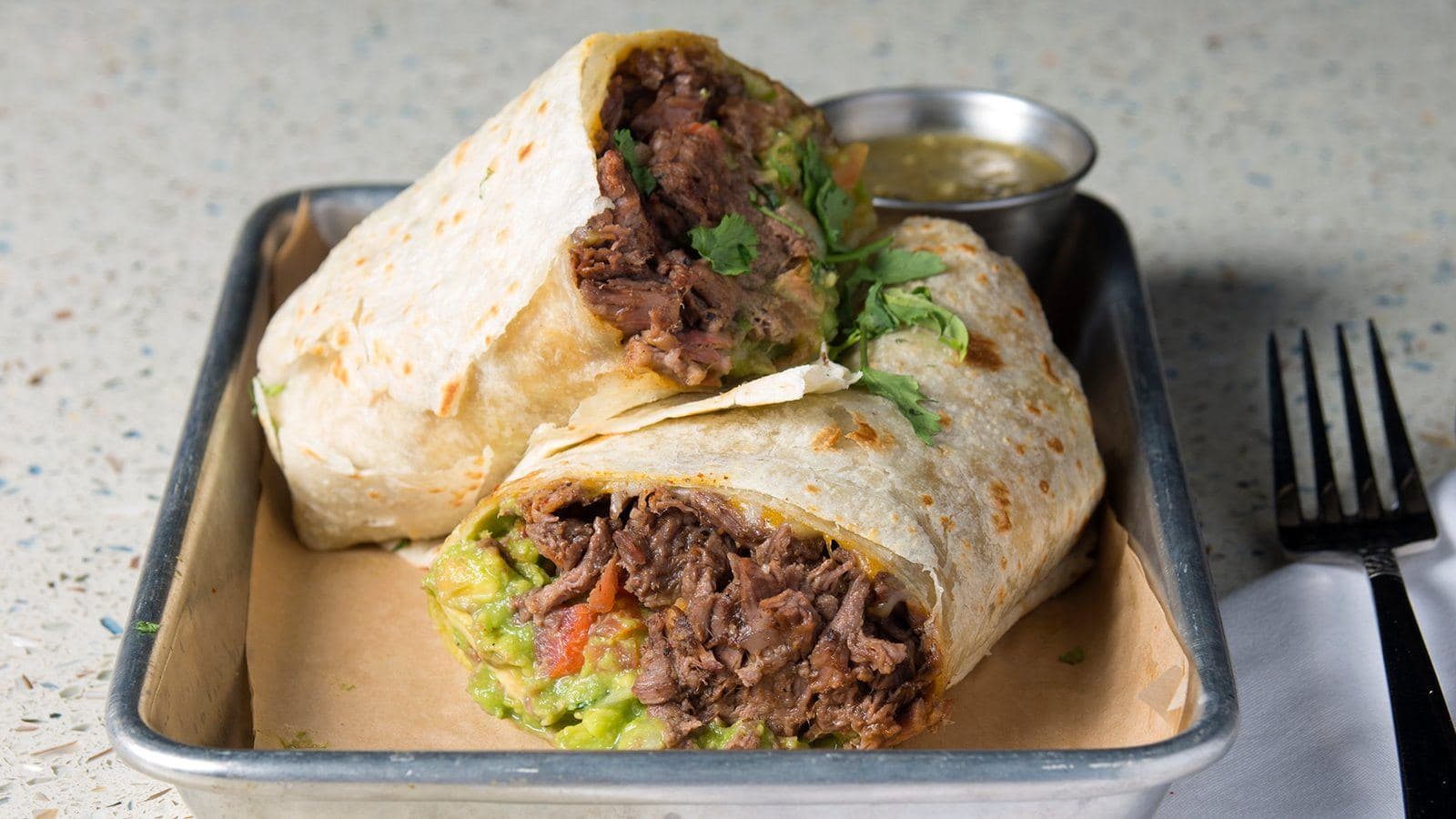 Carne asada burrito cut in half with guacamole and salsa verde
