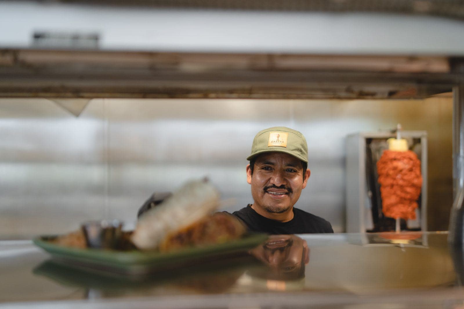 Cook at the kitchen pass with the al pastor trompo behind him