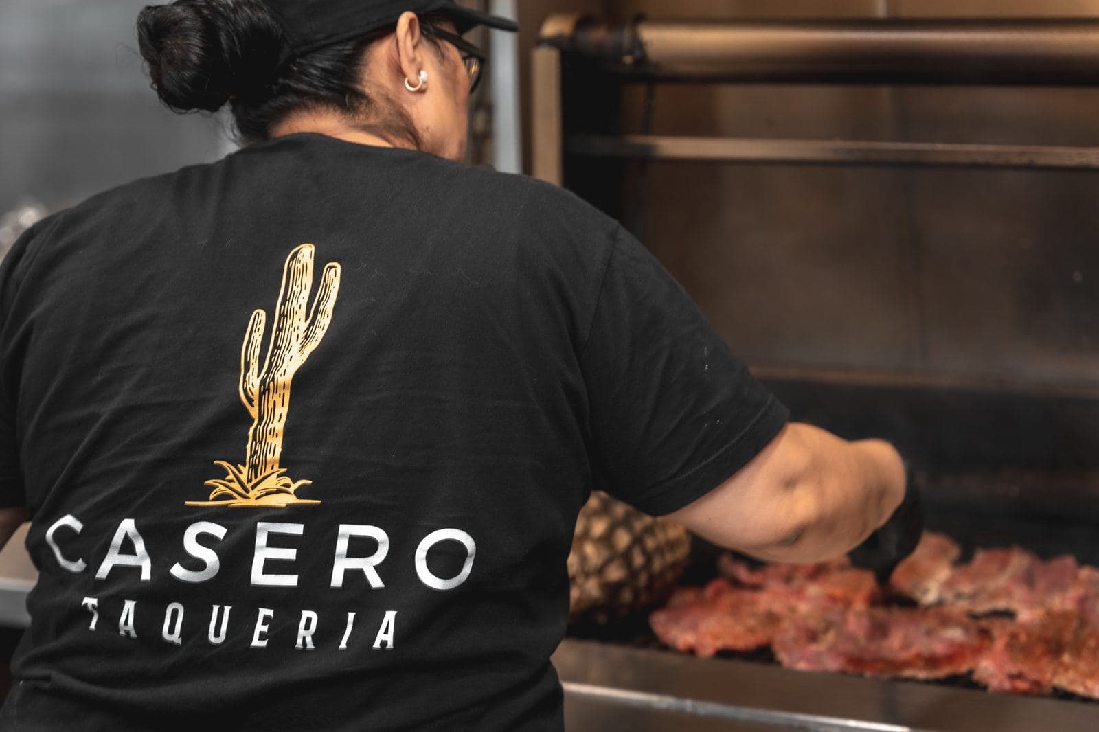Cook grilling carne asada in a Casero Taqueria shirt